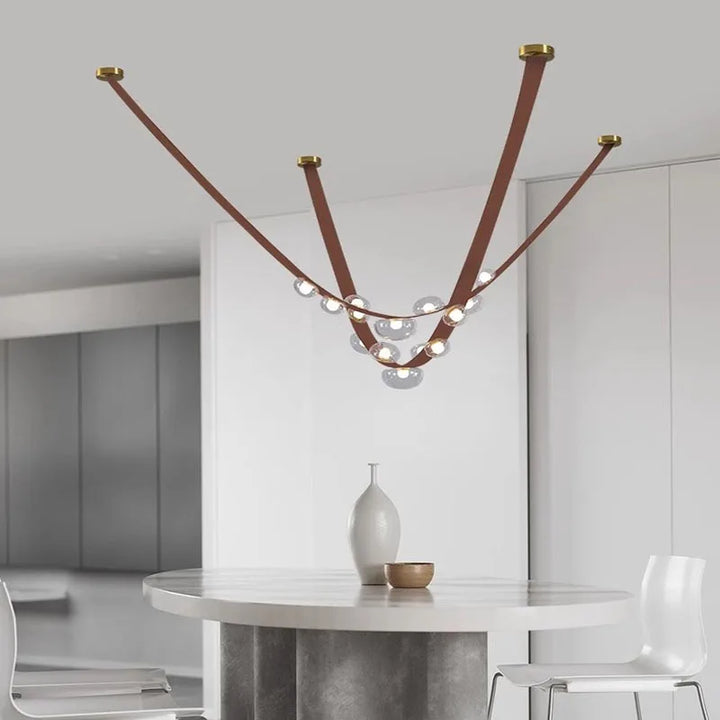 Suspension minimaliste en cuir marron clair et sphères lumineuses transparentes, valorisant un espace de vie moderne.