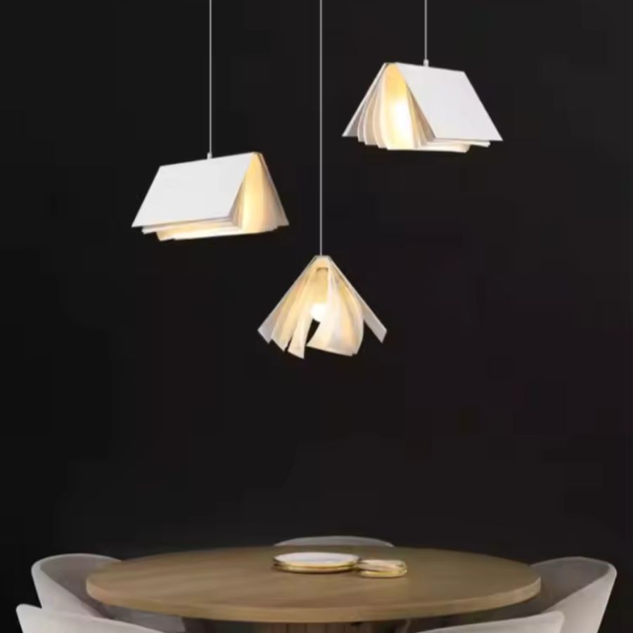 Trio de suspensions design en forme de livre ouvert au-dessus d’une table, dans un style minimaliste et contemporain