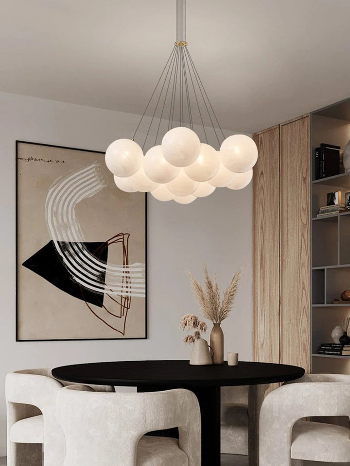 Suspension design en grappe de globes en verre opalin blanc, suspendus par câbles fins avec finition laiton.