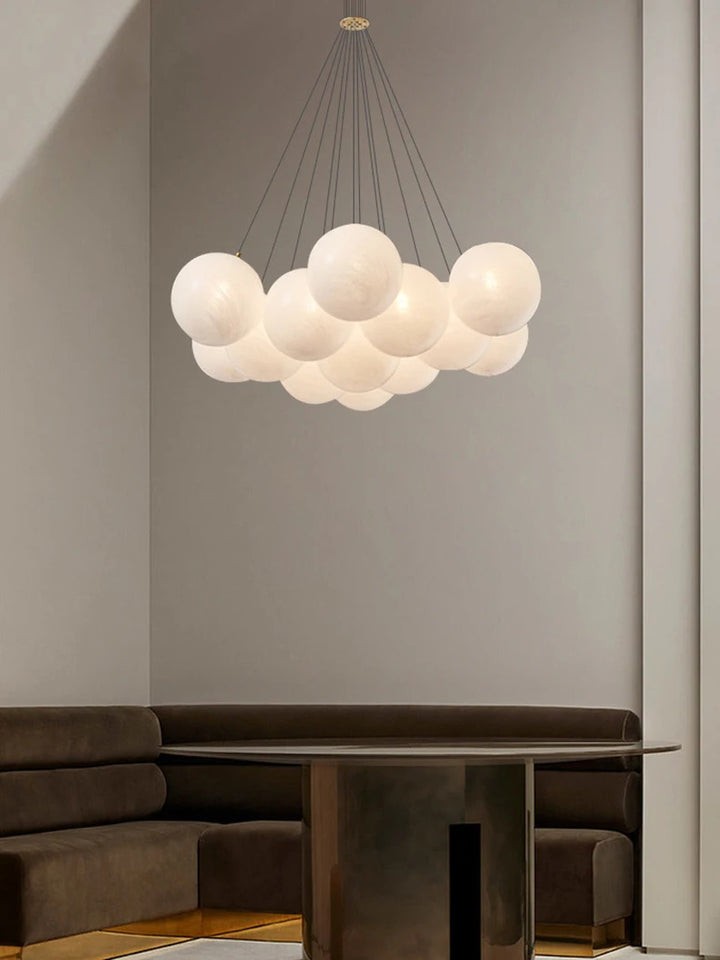 Suspension design en grappe de globes en verre opalin blanc, suspendue par de fins câbles pour un rendu aérien.