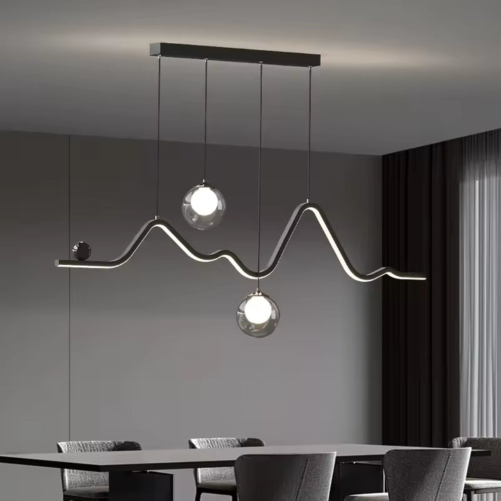 Une suspension à ligne LED ondulée et deux globes en verre illumine une salle à manger au style moderne et sculptural.