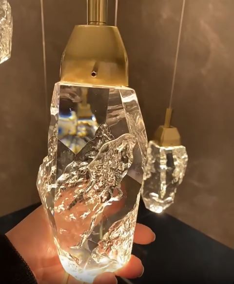 Gros plan sur le pendentif suspension diamant en verre type cristal facetté à monture dorée, diffusant un éclairage précieux et raffiné.