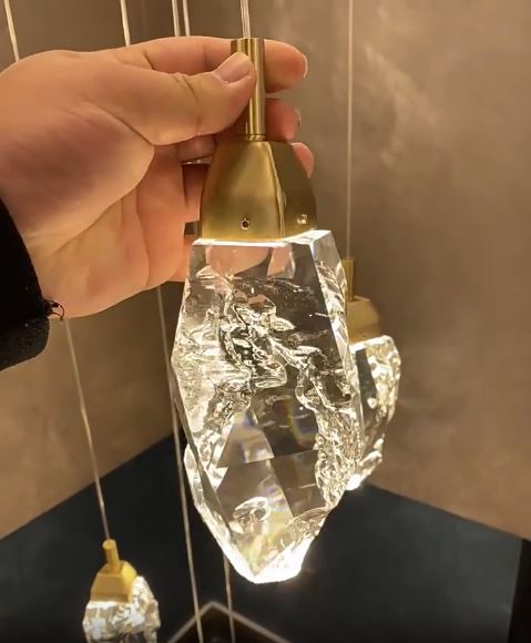 Gros plan sur un pendentif suspension diamant à monture dorée en verre type cristal, diffusant une lumière précieuse et raffinée.