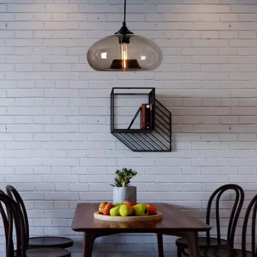 Au-dessus d’une table en bois, cette suspension dôme en verre fumé associe style vintage, industriel et contemporain