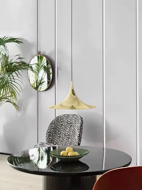 Suspension conique dorée miroir au-dessus d’une table noire, entre design italien, chic vintage et modernité sculpturale.