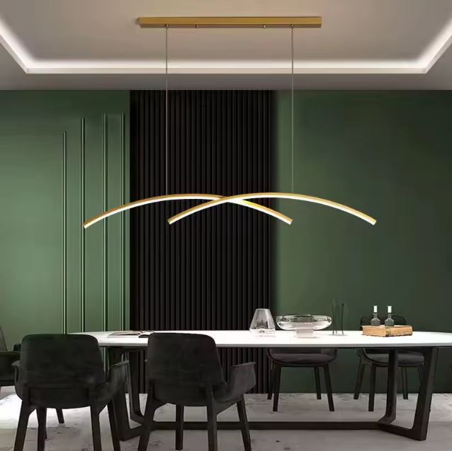 Suspension double arc LED dorée éclairant une salle à manger élégante avec un mur vert et une table moderne.