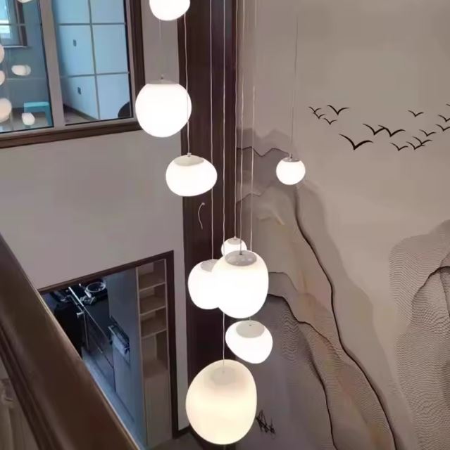Suspension escalier boule blanche à hauteurs variées, idéale pour illuminer une cage d’escalier moderne avec une ambiance douce et aérienne.
