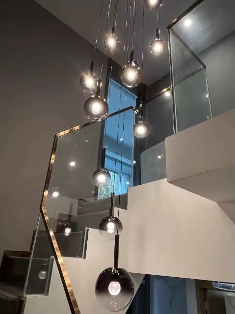 Suspension d’escalier en cascade, globes en verre fumé noir, ambiance loft contemporaine et lumineuse.