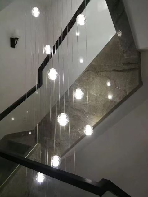 Suspension d’escalier à globes en verre bullé, lignes verticales épurées et éclairage design minimaliste.