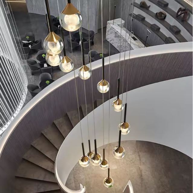 Suspension design noir et or à globes lumineux installée dans un escalier grande hauteur, idéale pour sublimer un intérieur moderne et élégant.