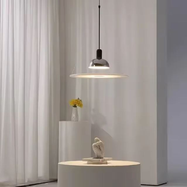 Suspension fine chromée dans un décor blanc minimaliste, parfaite pour un éclairage doux et épuré.