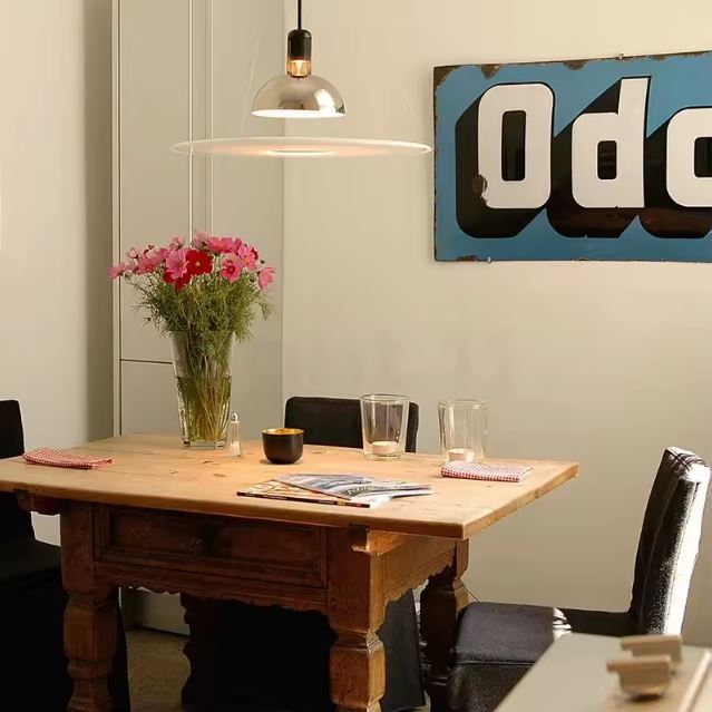 Suspension fine chromée au-dessus d’une table vintage en bois, parfaite pour une salle à manger éclectique et chaleureuse.