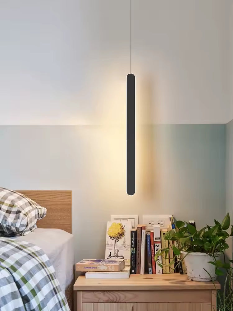 Près du lit, une fine et longue suspension noire au contour lumineux diffuse un éclairage doux dans une chambre minimaliste