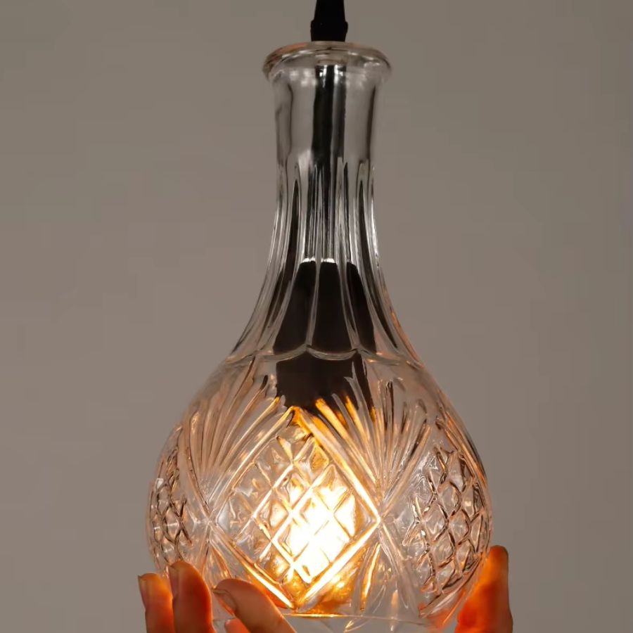 Gros plan sur une suspension flacon en verre transparent taillé, aux motifs rétro et à la lumière chaude décorative