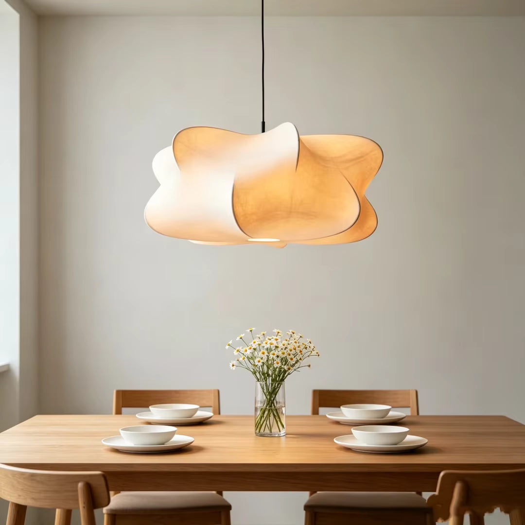 Une suspension aux pétales ondulants blanc ivoire illumine une table en bois, dans une salle à manger au style scandinave épuré.
