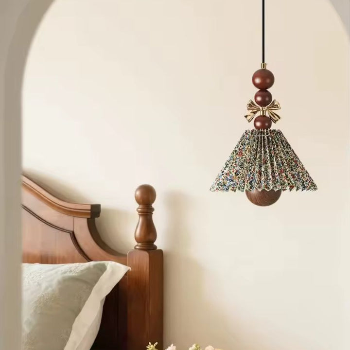 Au-dessus d’un lit en bois, la suspension florale plissée mêle tissu imprimé, perles brunes et nœud doré au style rétro