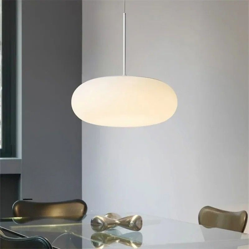 Suspension design moderne en verre opalin blanc en forme de galet suspendue au-dessus d'une table.