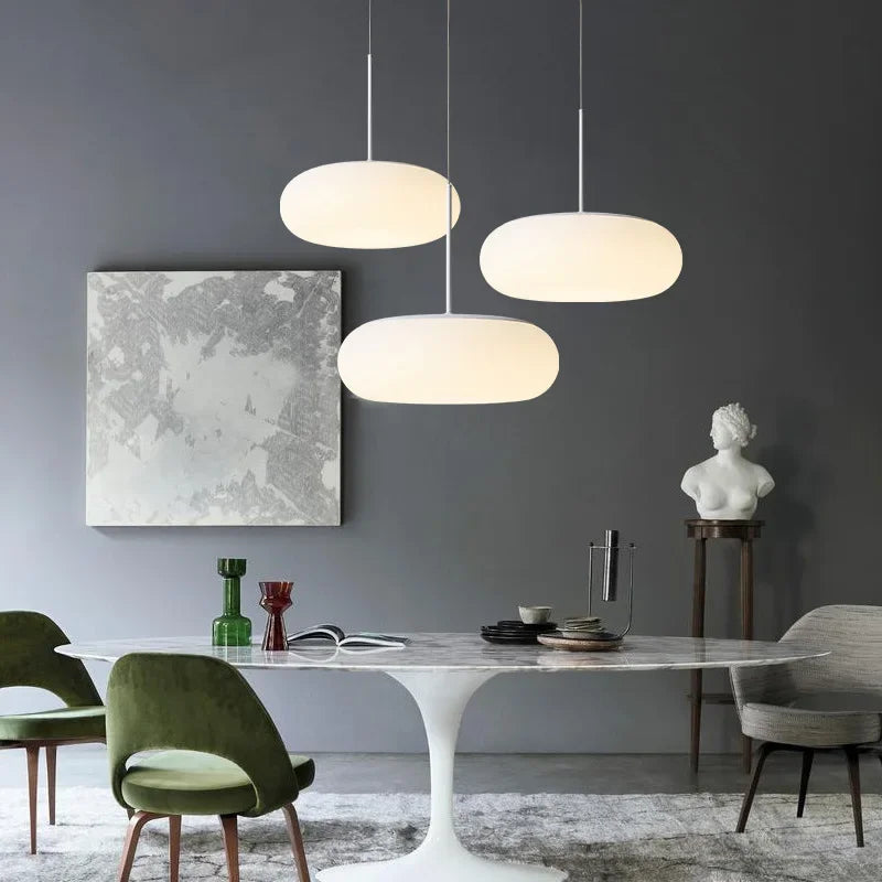 3 suspensions design galet en verre opalin blanc éclairant une table à manger moderne.