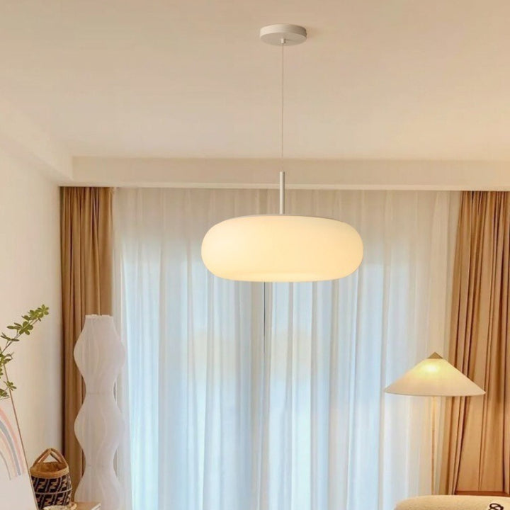 Abat-jour suspendu galet flottant en opaline blanche diffusant un halo chaleureux.