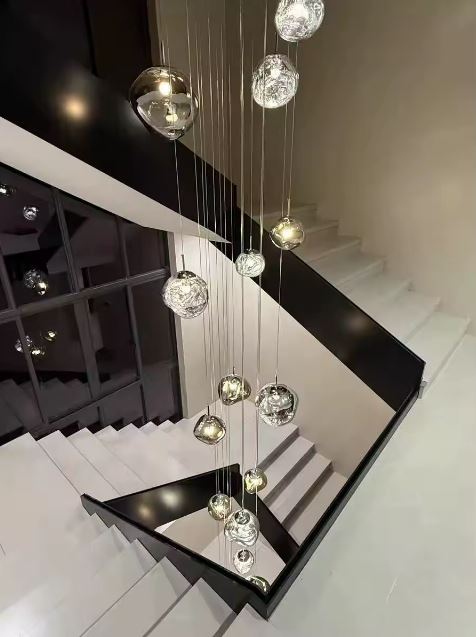 Suspension galets effet miroir en cascade dans un escalier moderne, luminaire sculptural idéal pour grande hauteur.