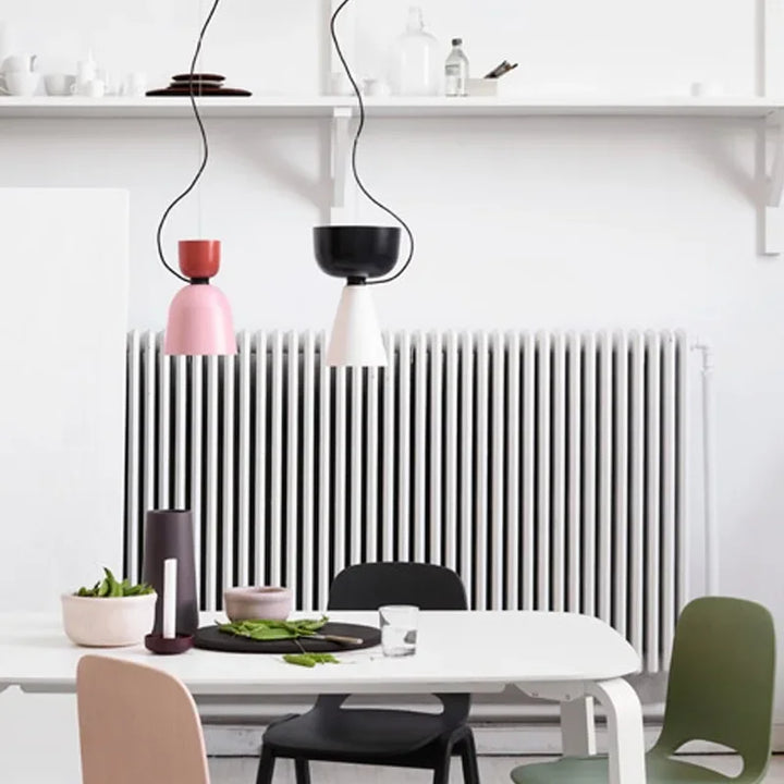 Vue d'ambiance d'une salle à manger lumineuse mise en valeur par deux élégantes suspensions design de fore géométrique en métal coloré.