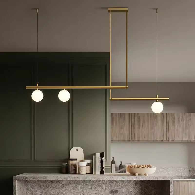 Structure dorée à lignes décalées et trois globes opalins, suspendue dans une cuisine contemporaine raffinée