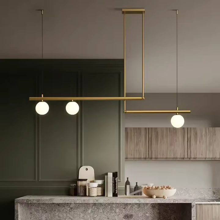 Structure dorée à lignes décalées et trois globes opalins, suspendue dans une cuisine contemporaine raffinée