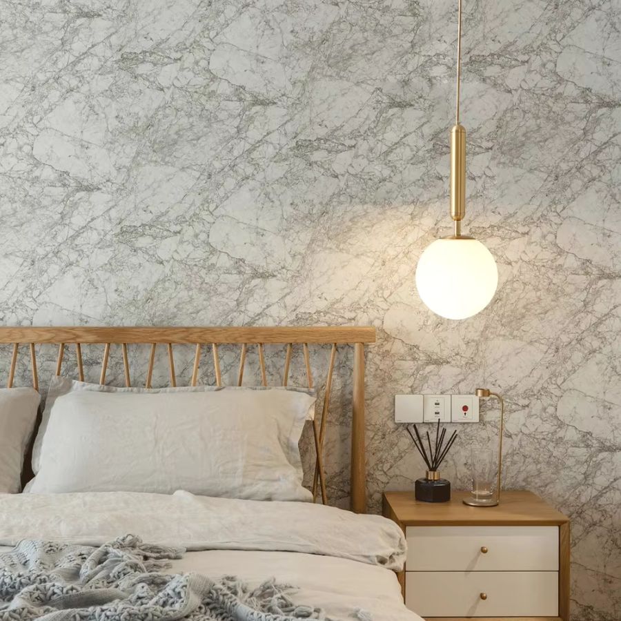 Suspension globe opalin à tige dorée au-dessus d’une table de chevet, dans une chambre naturelle au style japandi épuré