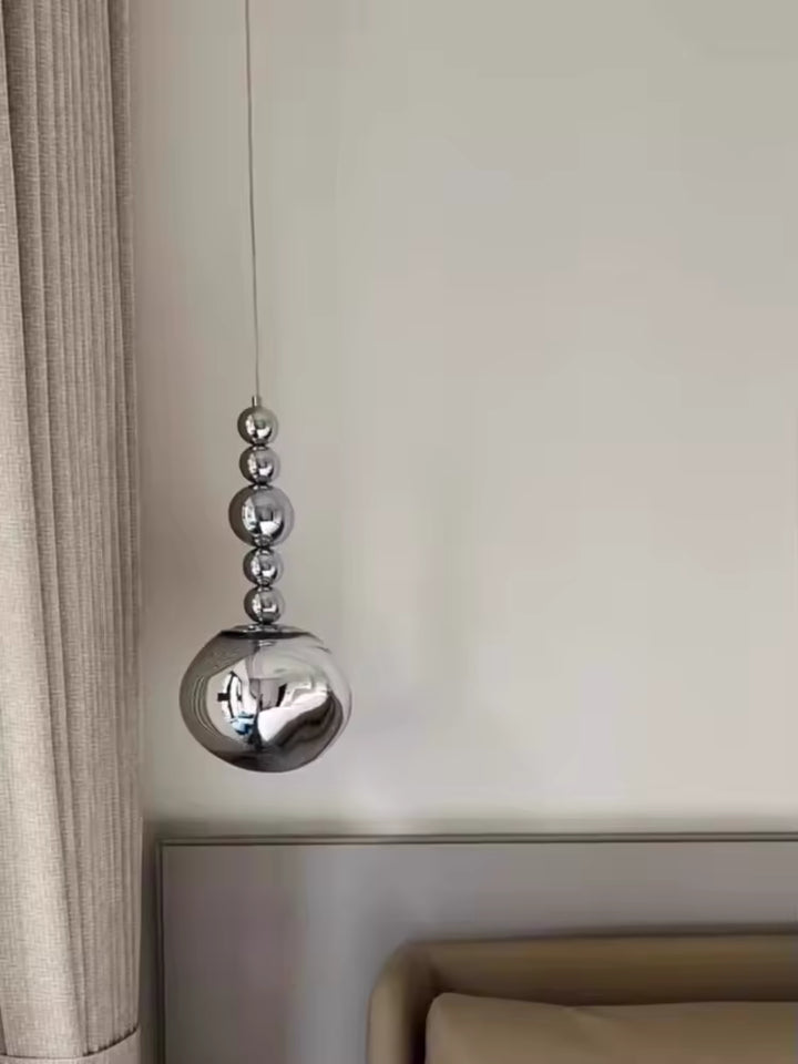 Près du lit, un globe fumé aux reflets miroir s’associe à cinq sphères chromées dans une suspension contemporaine