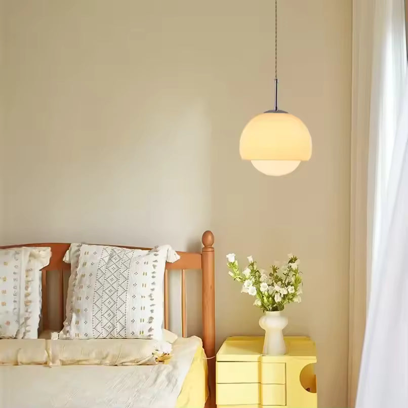 Dans une chambre douce, suspension beige à globe opalin au style rétro et aux lignes arrondies