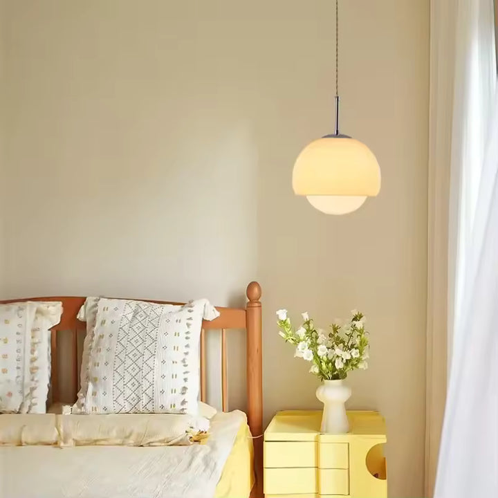 Dans une chambre douce, suspension beige à globe opalin au style rétro et aux lignes arrondies