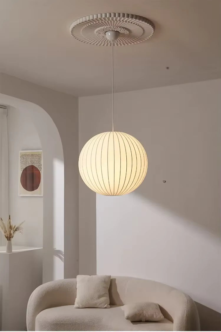Suspension globe en soie blanche plissée au style cocooning et minimaliste, diffusant une lumière chaleureuse dans le salon
