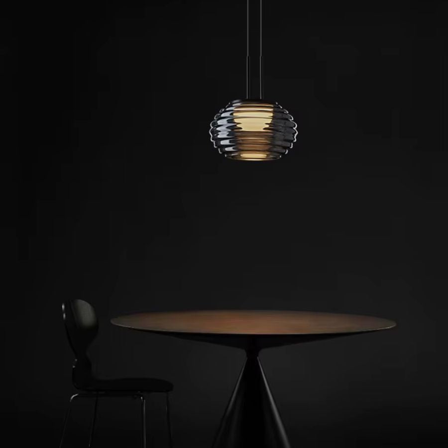 Suspension globe strié en verre fumé diffusant une lumière chaude dans une ambiance sombre et contemporaine