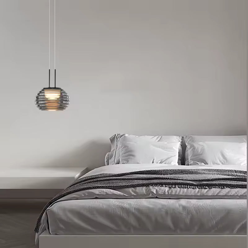 Suspension globe strié en verre fumé au style minimaliste, installée près d’un lit dans une chambre épurée