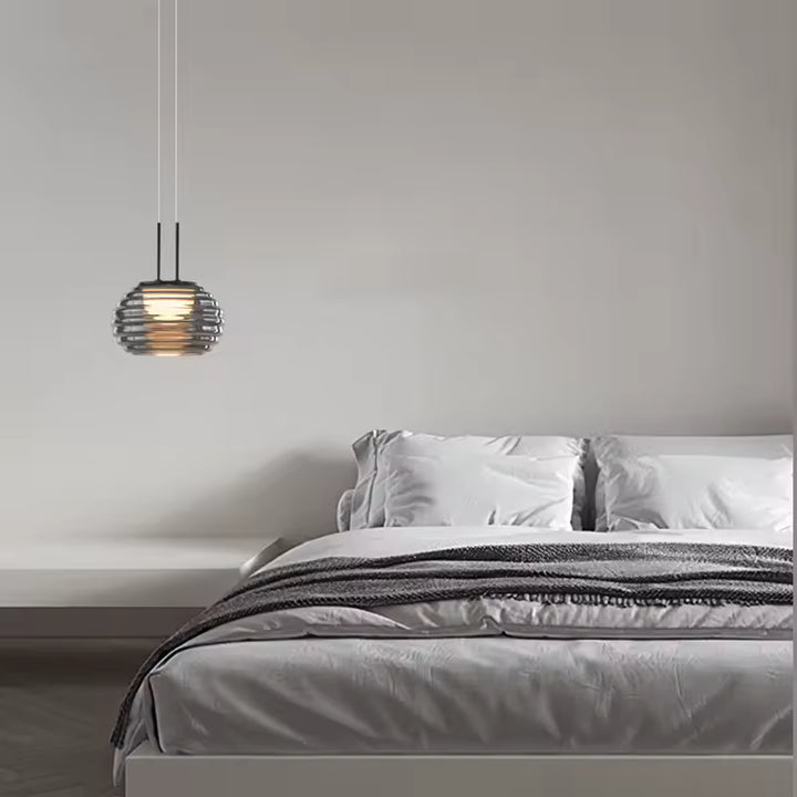 Suspension globe strié en verre fumé au style minimaliste, installée près d’un lit dans une chambre épurée