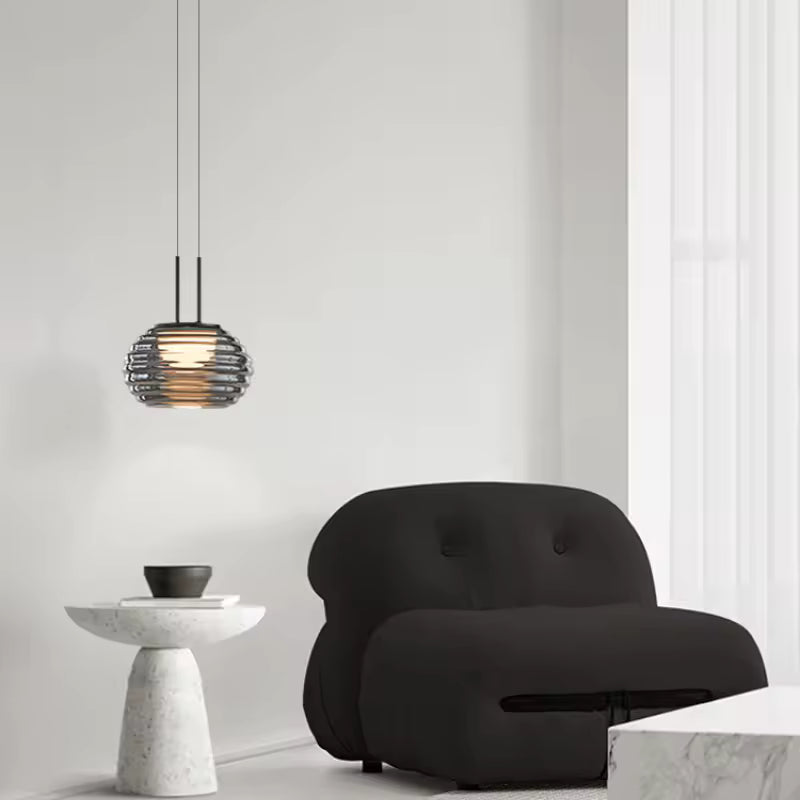 Suspension globe strié en verre fumé au style minimaliste, installée près d’un fauteuil dans un salon épuré