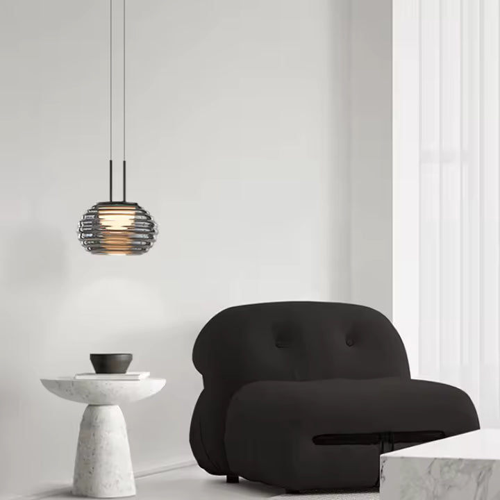 Suspension globe strié en verre fumé au style minimaliste, installée près d’un fauteuil dans un salon épuré