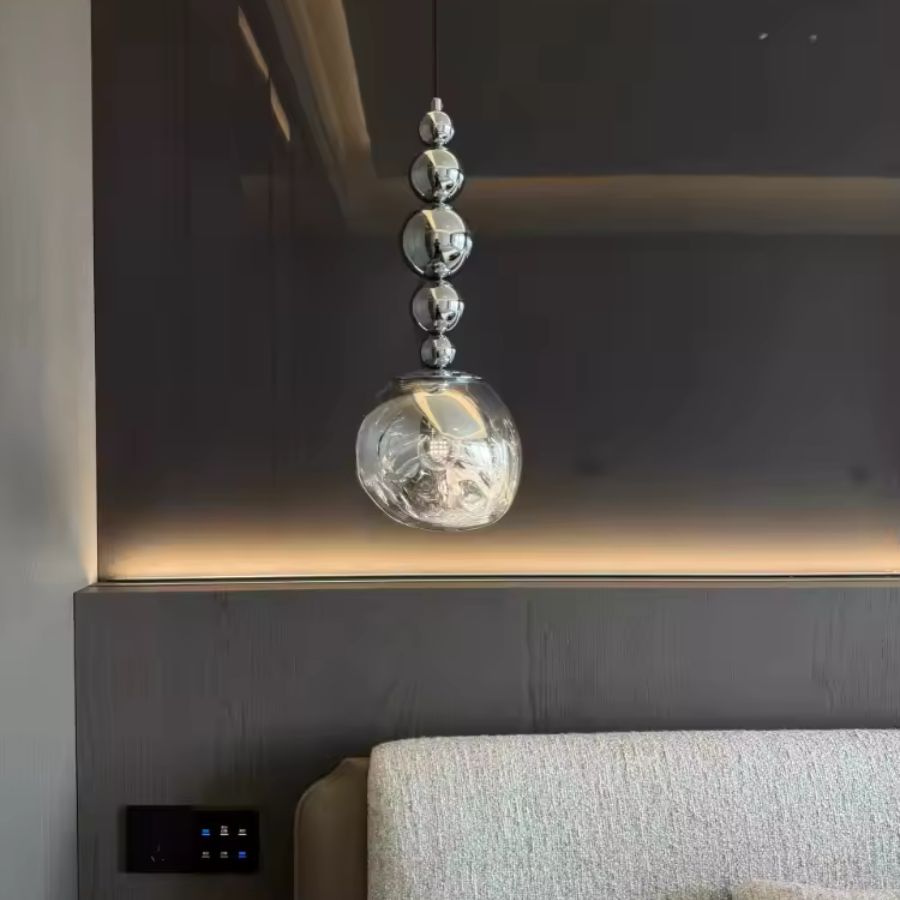 Au-dessus du chevet, cette suspension à sphères chromées et globe texturé apporte une présence chic et contemporaine