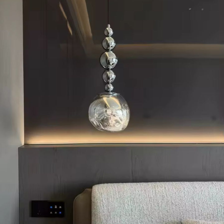 Au-dessus du chevet, cette suspension à sphères chromées et globe texturé apporte une présence chic et contemporaine