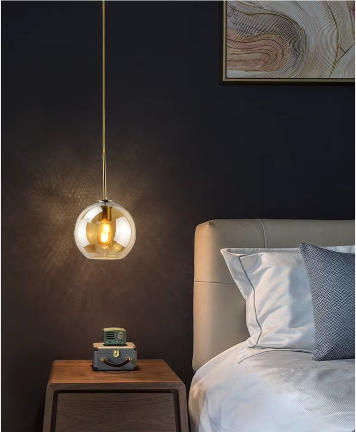 Suspension globe en verre ambré à ampoule apparente utilisée en chevet dans une chambre chic contemporaine