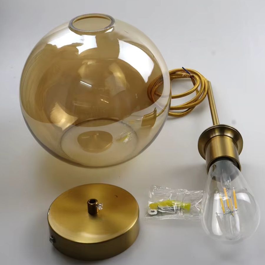 Globe en verre ambré associé à une structure dorée et une ampoule visible, dans un esprit décoratif raffiné