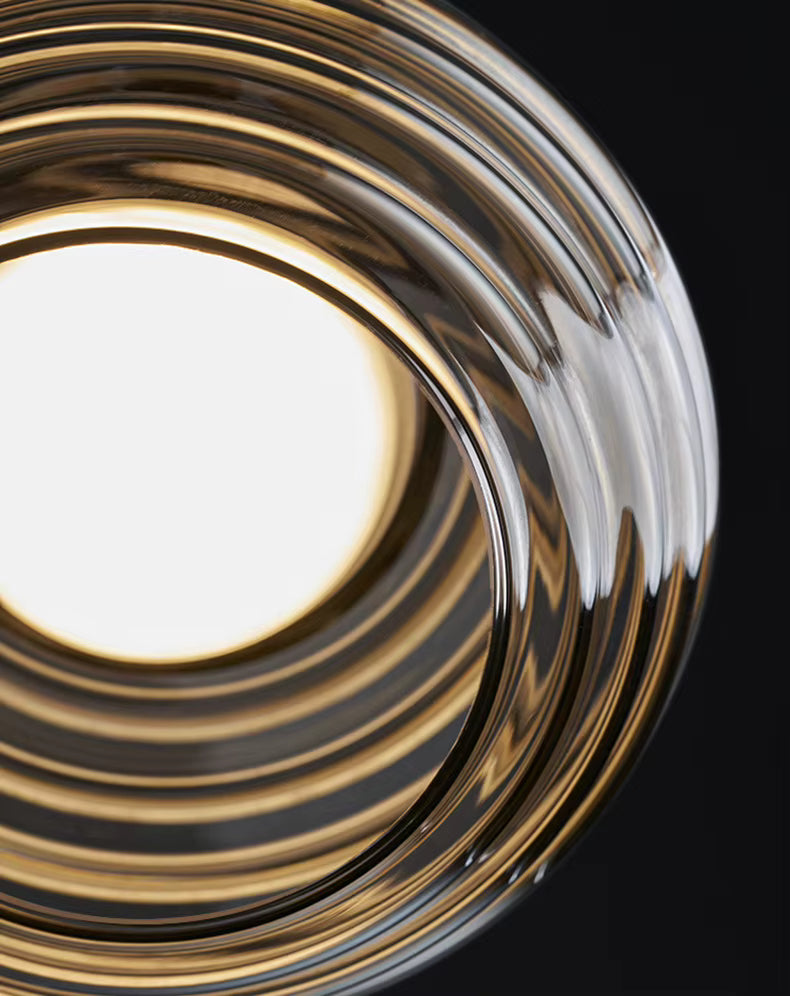 Vue rapprochée du verre fumé strié de la suspension, révélant ses reliefs concentriques et sa lumière chaleureuse
