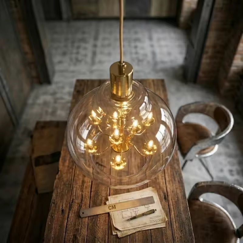 Globe en verre transparent avec lustre doré lumineux, suspendu au-dessus d’une table en bois dans un décor loft