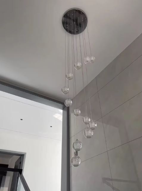 Suspension asymétrique de globes en verre bullé pour plafond haut, luminaire design épuré et contemporain.