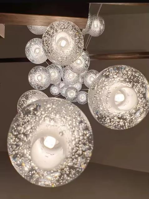 Détail de suspension à globes en verre bullé effet cristal, éclairage design haut de gamme et ambiance raffinée.