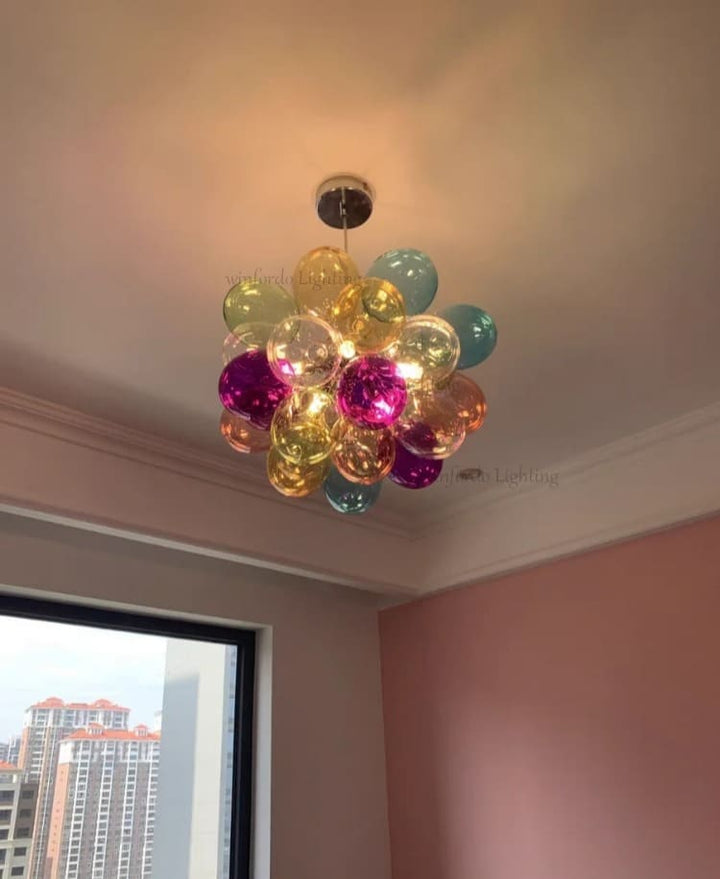 Luminaire suspendu en verre translucide multicolore créant des jeux de lumière colorés au plafond.
