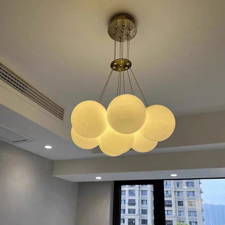 Suspension design allumée à globes en verre opalin blanc, suspendue par des câbles réglables avec finition laiton.