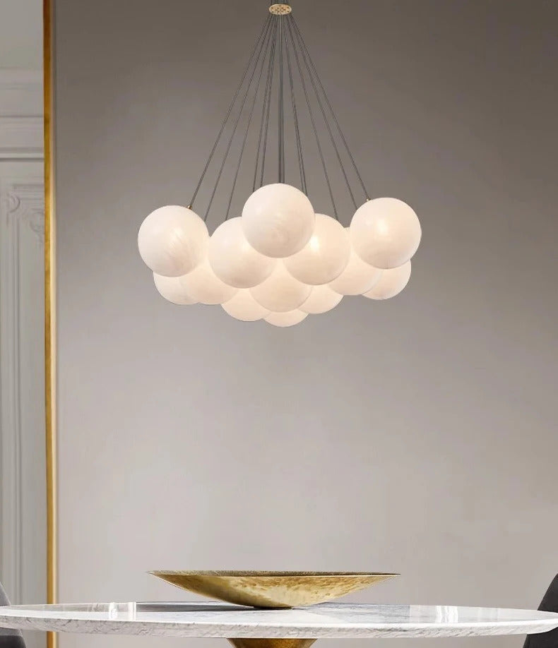 Vue d'ensemble d'une suspension design composée de globes en verre opalin blanc suspendus par de fins câbles.