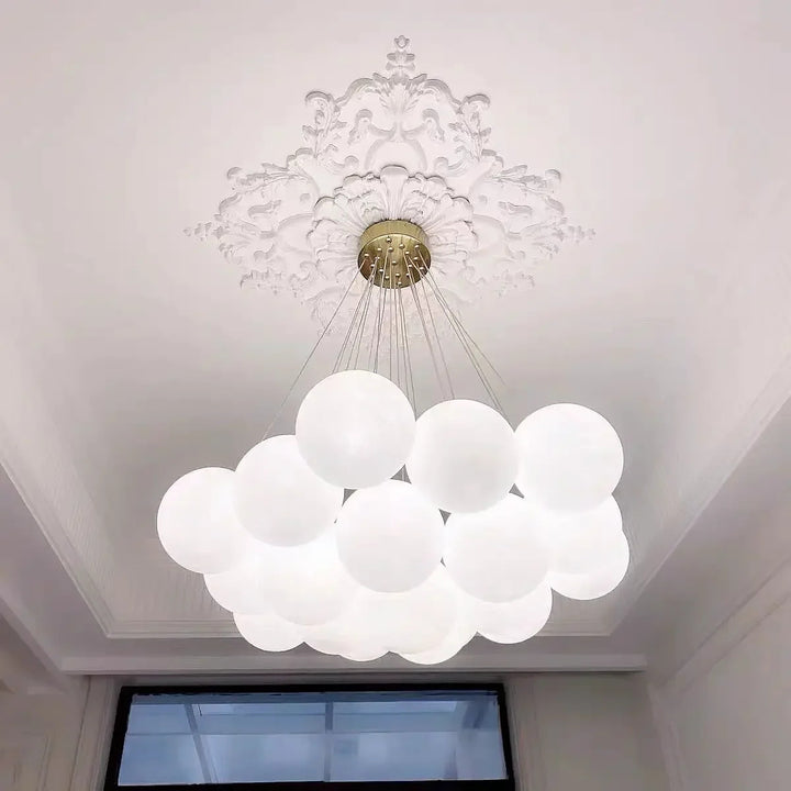 Suspension design à globes en verre opalin installée sous un plafond à moulures, alliant style contemporain et charme classique.