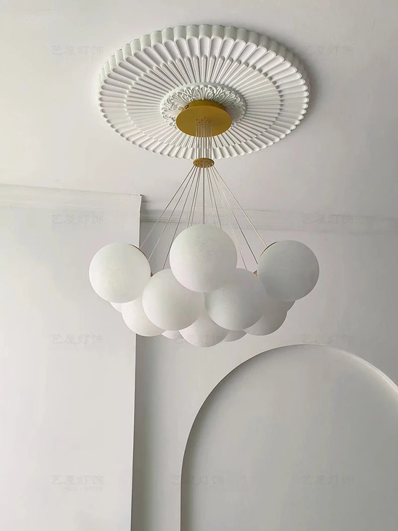Suspension design à globes en verre opalin blanc installée sous un plafond à moulures décoratives avec rosace en laiton.